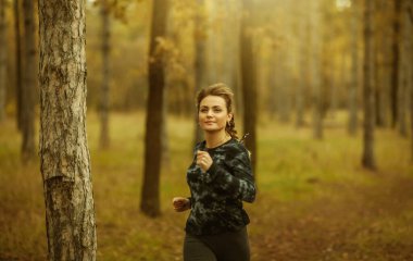 Sonbahar ormanında koşu. Spor giyimli genç bir kadın orman yolunda koşuyor. Sağlıklı yaşam tarzı kavramı