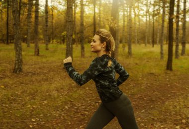 Sonbahar ormanında koşu. Spor giyimli genç bir kadın orman yolunda koşuyor. Sağlıklı yaşam tarzı kavramı