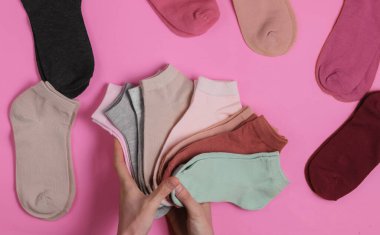 Pembe stüdyo arka planında bir yığın renkli çorap tutan kadın eli. Üst görünüm