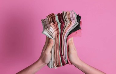 Pembe stüdyo arka planında bir yığın renkli çorap tutan kadın eli. Üst görünüm
