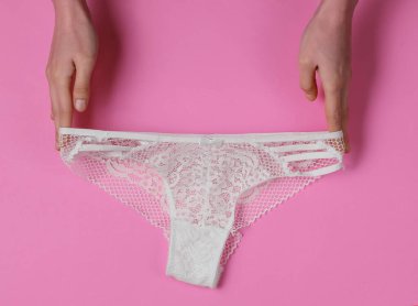 Kadın elleri pembe arka planda seksi dantel iç çamaşırları tutuyor. Stüdyo çekimi