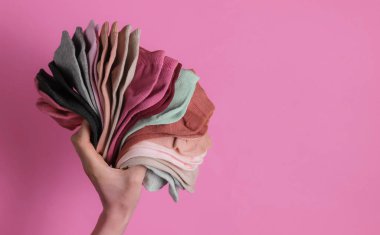Pembe stüdyo arka planında bir yığın renkli çorap tutan kadın eli. Üst görünüm