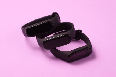 Pembe arka planda üç akıllı bilezik. Spor ve günlük aktiviteler için modern aletler