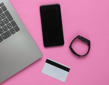 Laptop, akıllı telefon, akıllı bilezik ve pembe arka planda banka kartı. İnternetten alışveriş. Üst görünüm