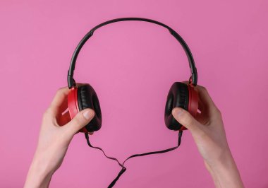 Kadın eli, pembe pastel arka planda şık telli kulaklık tutuyor. Müzik hayranı, DJ. Üst görünüm.