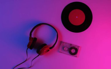 Kablolu kulaklıklar, vinil kayıt, neon mavi-kırmızı renkli ses kaseti. Retro dalga, 80 'lerin popüler kültürü. Üst görünüm