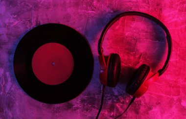 Kablolu kulaklıklar ve beton arka planda plaklar. Neon mavi-kırmızı eğimli ışık. Retro dalga, 80 'lerin popüler kültürü. Üst görünüm