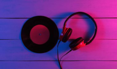 Kablolu kulaklıklar ve tahta arka planda plaklar. Neon mavi-kırmızı eğimli ışık. Retro dalga, 80 'lerin popüler kültürü. Üst görünüm