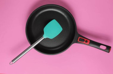 Pembe arka planda spatula pişirilmiş yapışmaz tava. Minimalizm kavramı pişirmek. Stüdyo çekimi. Üst görünüm