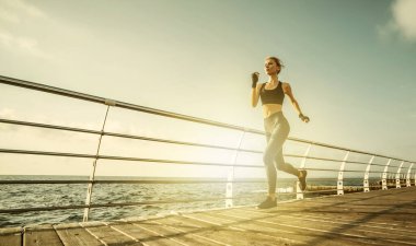 Sabah koşusu. Spor giyimli genç bir kadın güneş doğarken plajda koşuyor. Açık hava antrenmanı. Sağlıklı yaşam tarzı