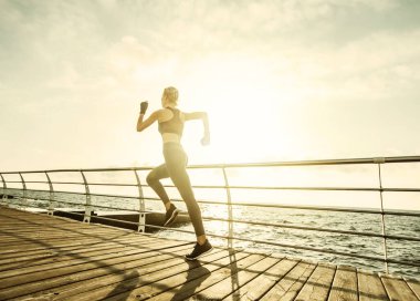 Sabah koşusu. Spor giyimli genç bir kadın güneş doğarken plajda koşuyor. Hızlı koşu. Sağlıklı bir yaşam tarzı. Arka plan