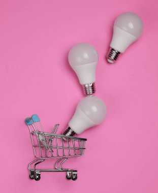 Pembe arka planda üç LED ampul ve alışveriş arabası. Üst görünüm