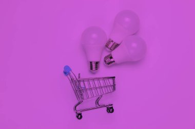 Üç LED ampul ve pembe neon ışıkta alışveriş arabası. Üst görünüm