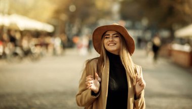 Paltolu ve şapkalı genç ve mutlu bir kadın şehirde dolaşıyor. Sonbahar zamanı