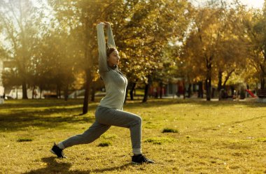Aerobik dışarıda çalışıyor. Spor giyimli genç bayan sonbahar parkında antrenman yapıyor..