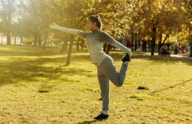 Genç sporcu kadın sonbahar parkında yoga yapıyor.