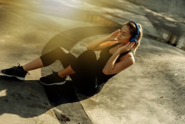 Spor giyimli çekici bir kadın spor salonunda otururken kulaklıkla müzik dinliyor.