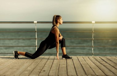 Eğitimden önce ısın. Mükemmel vücutlu zayıf genç bir kadın güneşli bir günde sahilde aerobik egzersizi yapıyor..
