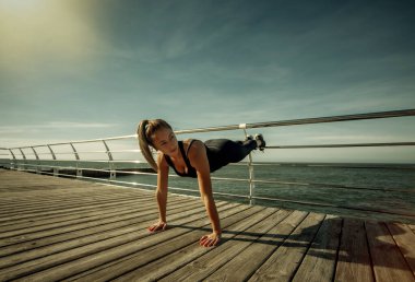 Eğitimden önce ısın. Mükemmel vücutlu zayıf genç bir kadın güneşli bir günde sahilde aerobik egzersizi yapıyor..
