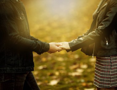 Romantik, aşk konsepti. Birbirine aşık genç bir çift, parkta düşen sonbahar yapraklarının bulanık arka planında el ele tutuşuyor. Romantik randevu