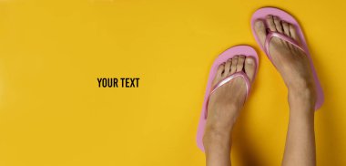 Plaj tatili için minimalist bir kavram. Sarı arka planda parmak arası terlikleri olan kadın bacakları. Uzayı kopyala Üst Manzara. Stüdyo çekimi