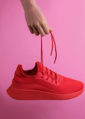 El, kırmızı spor ayakkabılarını pembe arka plandaki bağcıklardan tutuyor. Stüdyo çekimi