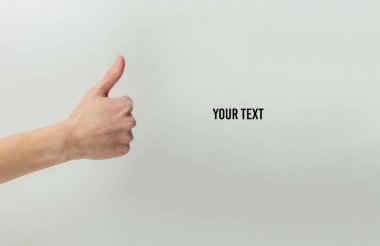 Kadın eli, beyaz bir arkaplanda metniniz için boşluk bırakarak başparmağını yukarı kaldırır