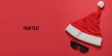 Kırmızı arka planda Noel Baba şapkası ve güneş gözlüğü. Yeni yıl, sıcak ve güneşli yerlerde Noel tatili. Plaj tatili Seyahat konsepti. Metnin için boşluk