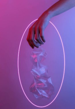 Geri dönüşüm konsepti. Kadın eli buruşuk plastik bir şişe tutuyor. Yaratıcı pop sanatının pembe neon rengi. Moda eğilimli aydınlatma. Gece lambası