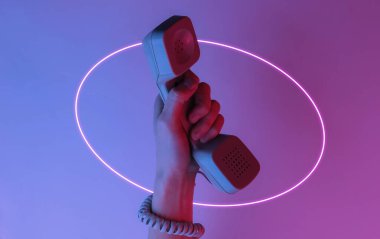 Kabloya sarılmış bir kadın el retro cep telefonunu tutuyor. Yaratıcı pop sanatı pembe neon renginde daire şeklinde. Moda eğilimli aydınlatma. Gece lambası