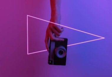 Kadın eli retro kamera tutuyor. Yaratıcı pop sanatının pembe neon rengi. Moda eğilimli aydınlatma. Gece lambası