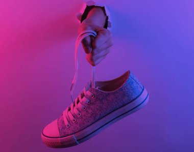 Yırtık delikten el ele tutuşan spor ayakkabısı. Yaratıcı pop sanatının pembe neon rengi. Moda eğilimli aydınlatma. Gece lambası