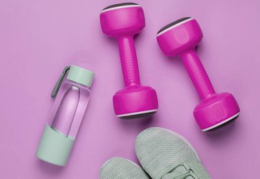 Düz konsept, sağlıklı yaşam tarzı, spor ve zindelik. Koşmak için spor ayakkabıları, dambıllar, pembe pastel arka planda bir şişe su. Üst görünüm