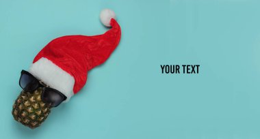 Yaratıcı yeni yıl, Noel konsepti. Mavi arka planda Noel Baba şapkası olan gözlük takmış ananas. Üst Manzara. Boşluğu kopyala