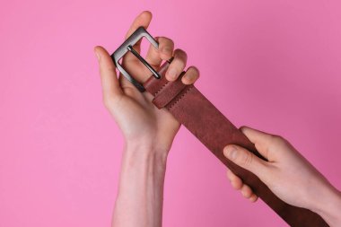 Kadının elinde pembe arka planda izole edilmiş kahverengi bir deri kemer var.