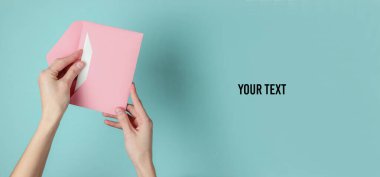 Kadının elinde mavi pastel arka planda bir zarf var. Üst Manzara. Sevgililer günü, düğün davetiyesi, aşk mektubu.