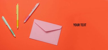 Turuncu arka planda zarf ve renkli kalemler. Üst Manzara. Boşluğu kopyala