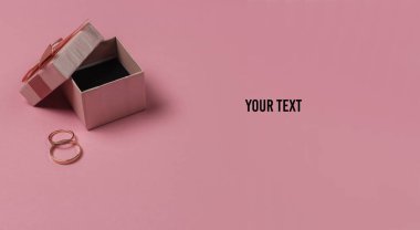 Pembe pastel arka planda yay ve altın yüzüklü hediye kutusu. Düğün konsepti. Mücevherler. Boşluğu kopyala
