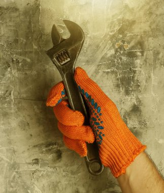 İş eldivenli eller gri beton arka planda ingiliz anahtarı tutuyor. Sanayi işçisi