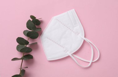K95 tıbbi maske ve pembe arka planda okaliptüs. Üst görünüm