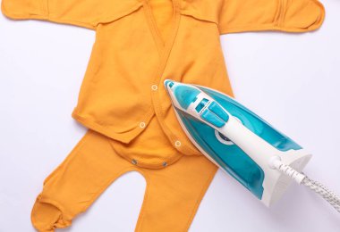 Beyaz arka planda yeni doğmuş bebeğin kıyafetlerini ütüleyen demir.