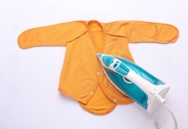 Beyaz arka planda yeni doğmuş bebeğin kıyafetlerini ütüleyen demir.