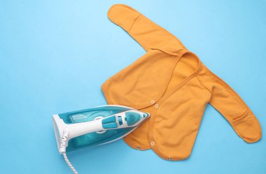 Mavi arka planda yeni doğmuş bebeğin kıyafetlerini ütüleyen demir.