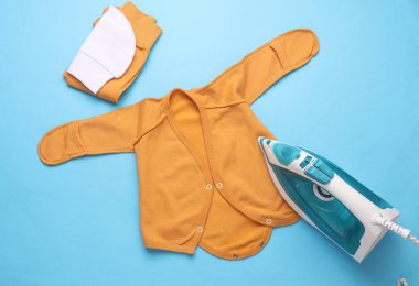 Mavi arka planda yeni doğmuş bebeğin kıyafetlerini ütüleyen demir.