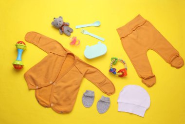 Sarı arka planda yeni doğmuş bebek kıyafetleri, aksesuarlar ve oyuncaklar. Düz yatıyordu. Üst görünüm