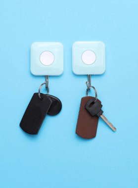 Mavi arka planda asılı manyetik ve metal tuşlu deri anahtarlıklar.