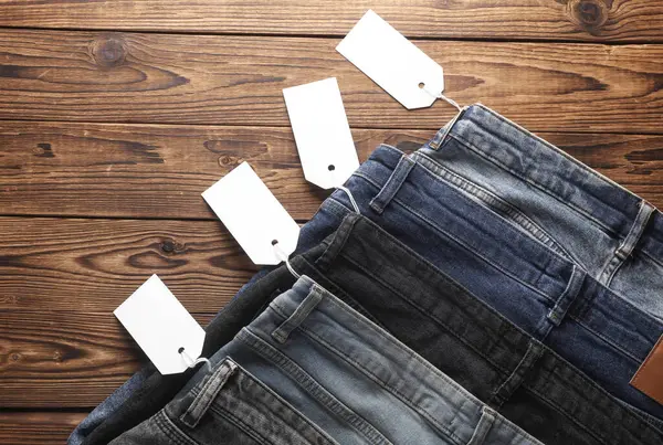 Ahşap arka planda beyaz etiketli bir sürü kot pantolon. Üst görünüm