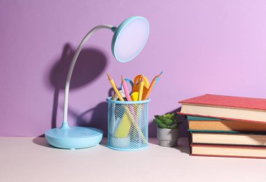 Masa lambası, kırtasiye malzemeleri, mor arka plan kitapları. Eğitim kavramı