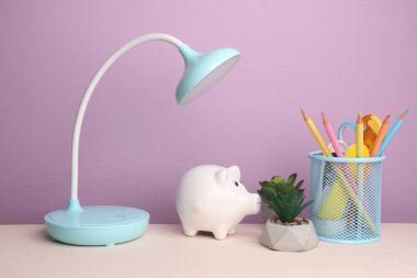 Masa lambalı domuz kumbarası ve mor arka planda kırtasiye malzemesi