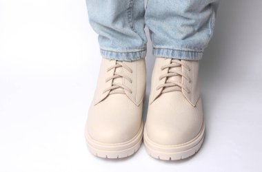 Kot pantolonlu kadın bacakları ve beyaz arka planda beyaz deri çizmeler. Moda konsepti